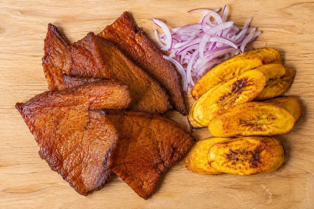 Strips of smoked and dried Peruvian cecina on a wooden board with green plantains and lime