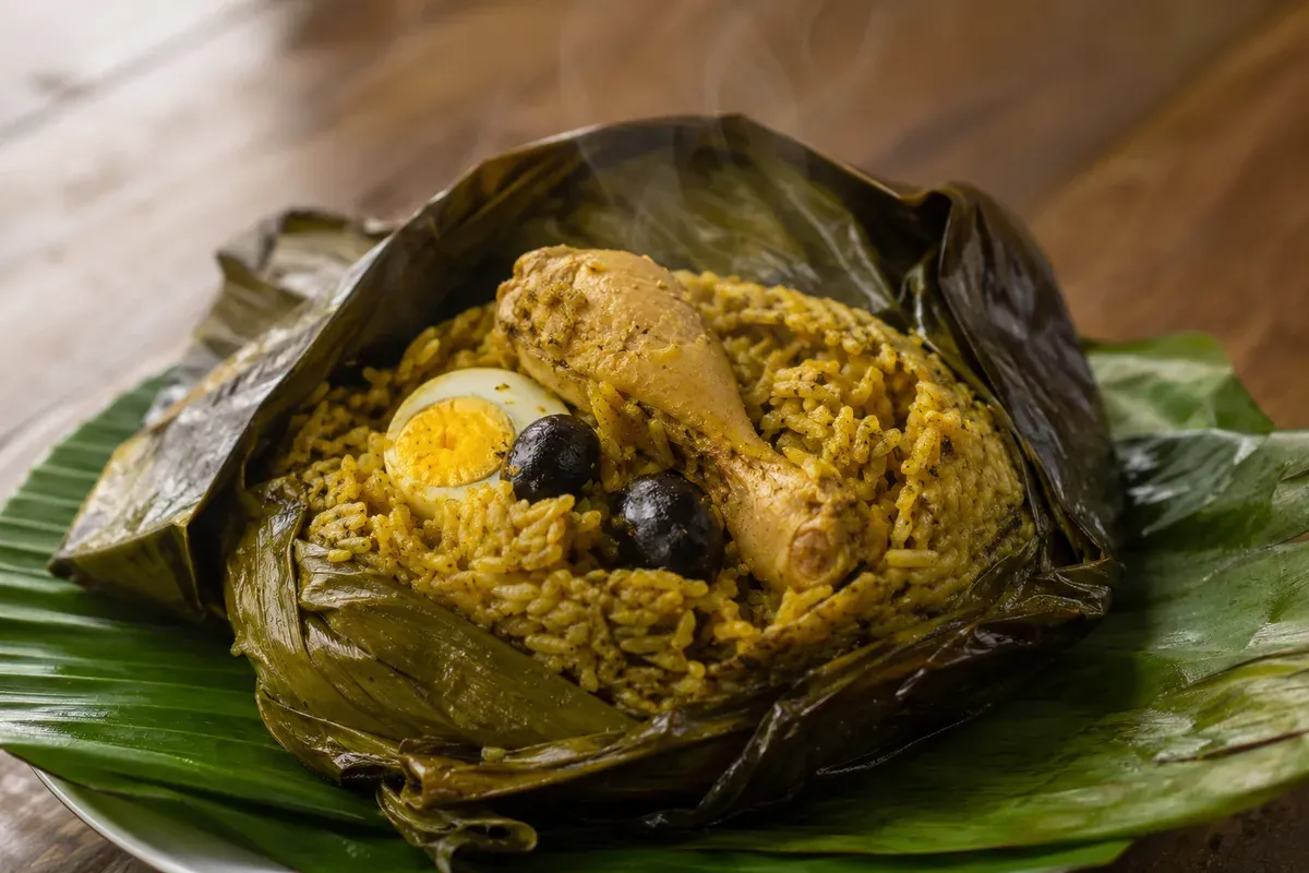 A juane unwrapped at the table: golden turmeric rice with chicken, boiled egg and olives inside bijao leaves