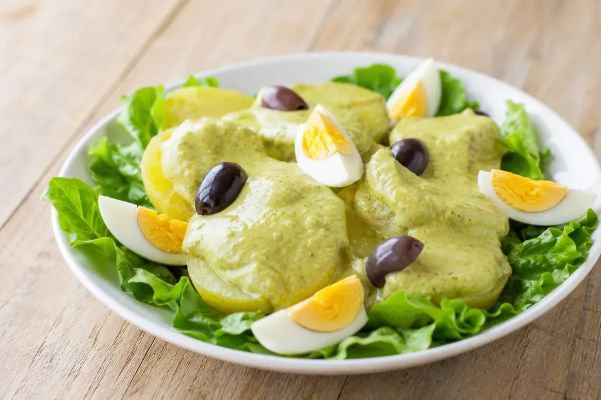 Boiled potato slices under thick olive-green ocopa sauce with egg and olives